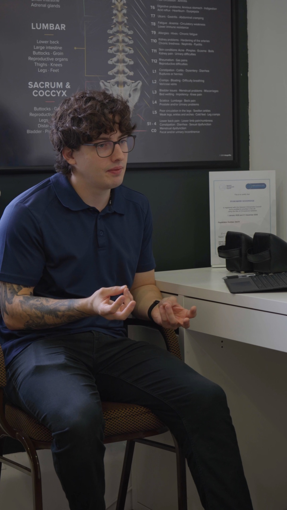 A chiropractor sitting at a desk, mid-explanation, hands raised