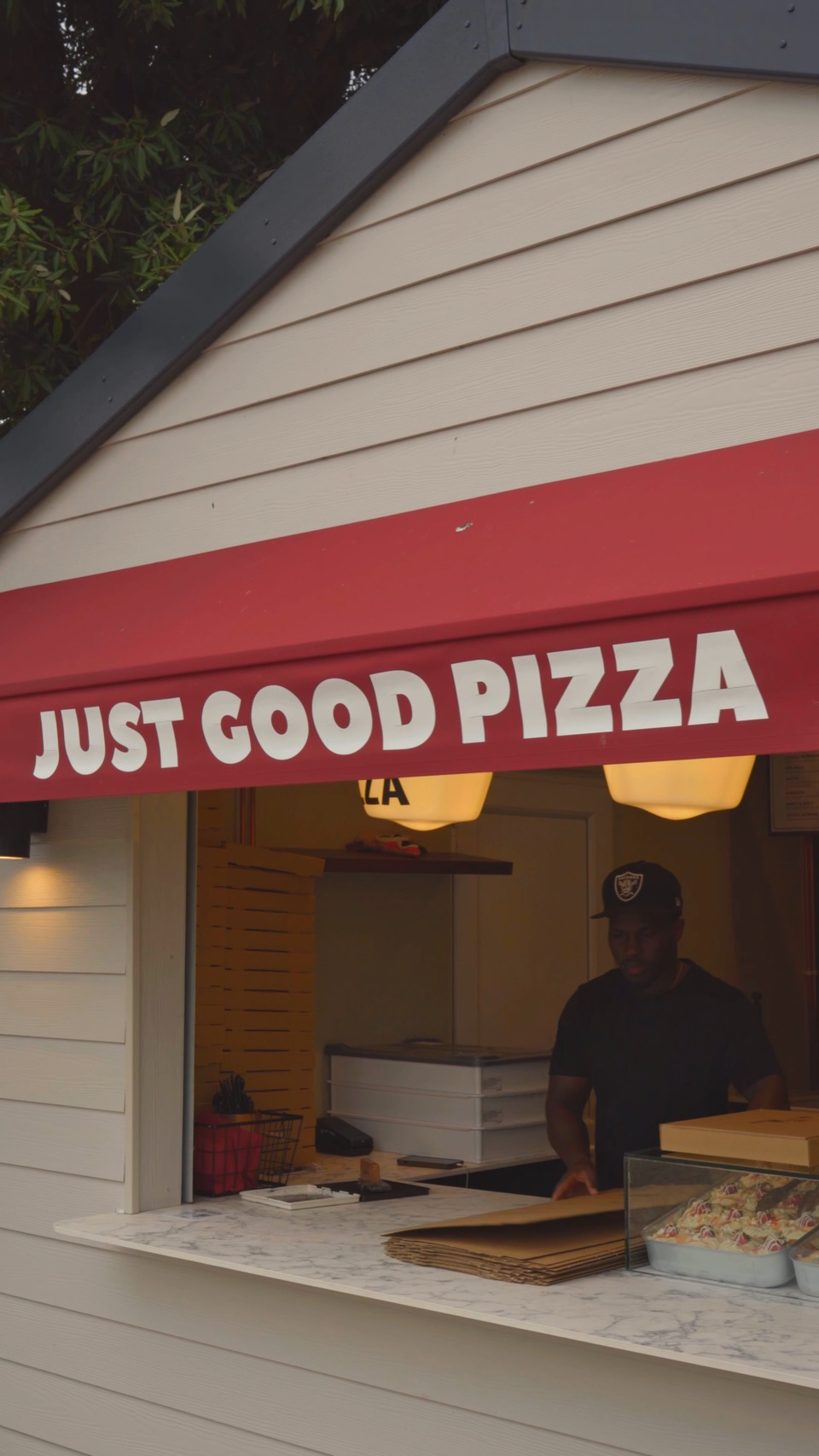 The red awning lettered Just Good Pizza, with a member of staff at the serving hatch