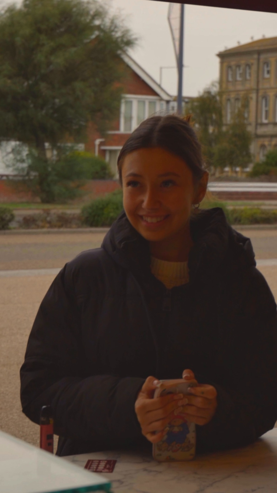 A customer in a black coat smiling at a table outside