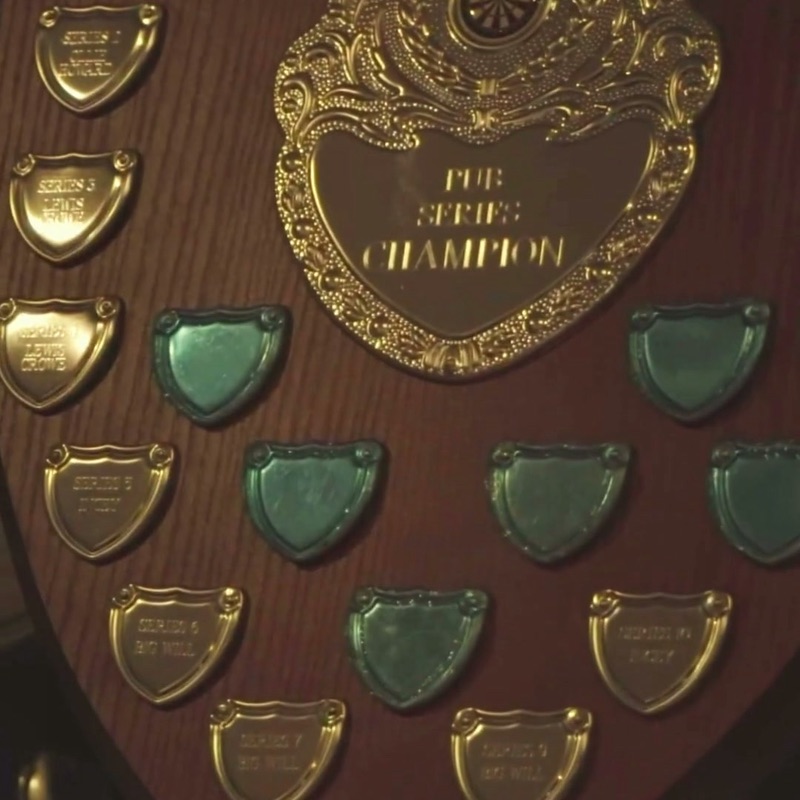 A wooden trophy shield with a gold plate reading “Pub Series Champion” and rows of small engraved shields