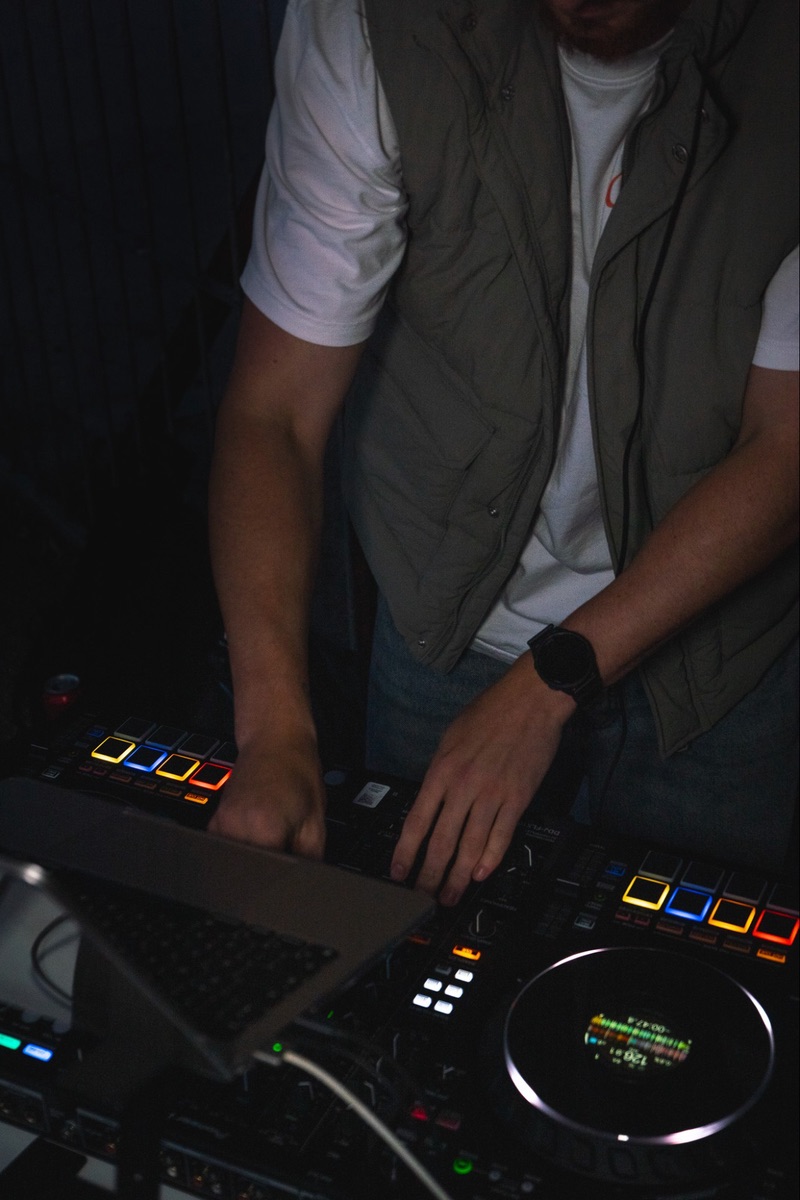 The DJ's hands on the controller in the dark, its pads lit orange, blue and yellow