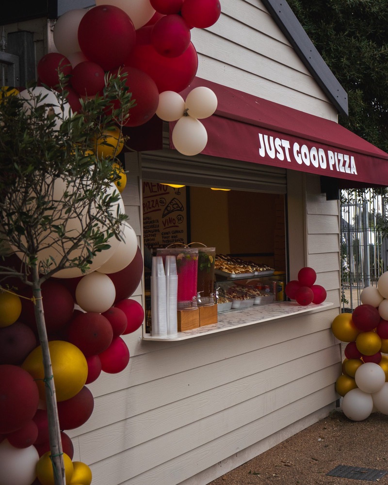 The serving hatch dressed with red, gold and white balloons, an olive tree beside it