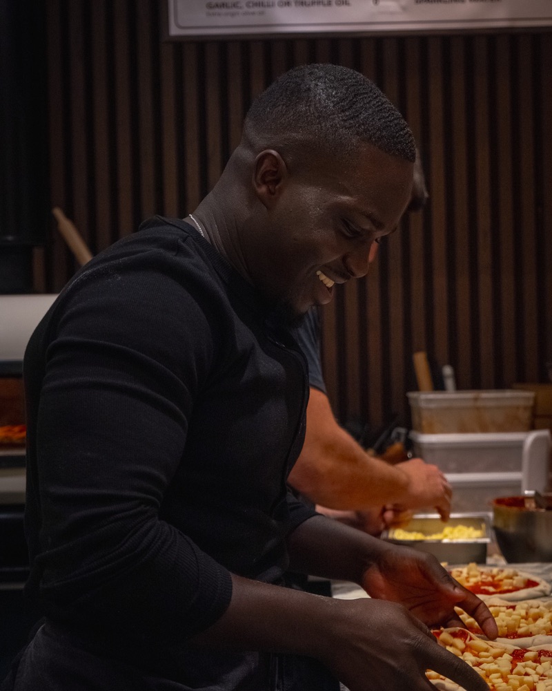 One of the team laughing as he tops pizza bases with cheese