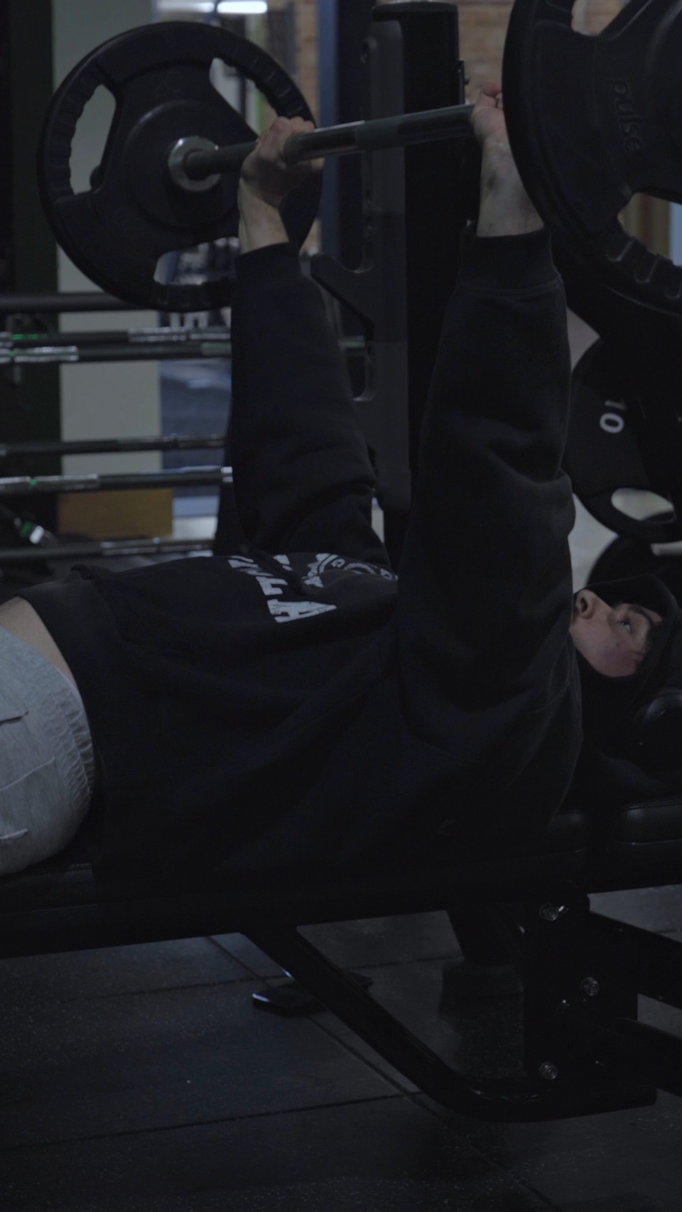 Someone in a black hoodie bench-pressing a loaded barbell