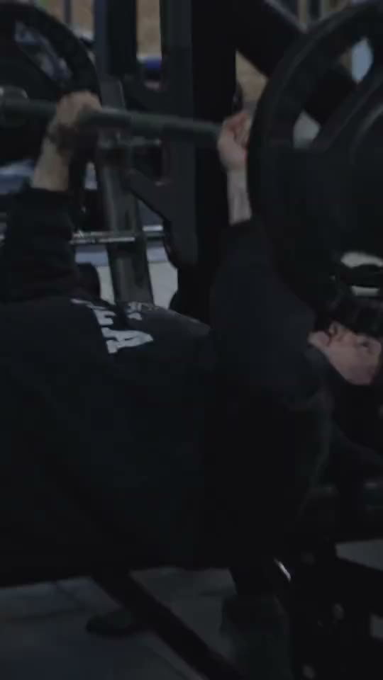 Someone bench-pressing a loaded barbell in a dark gym