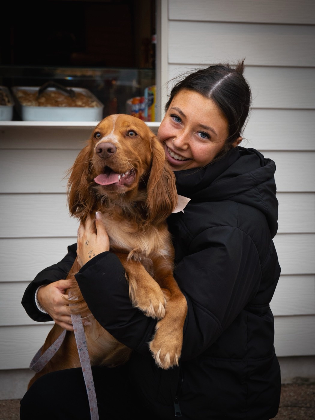 A customer smiling at the camera, holding a cocker spaniel at the serving hatch