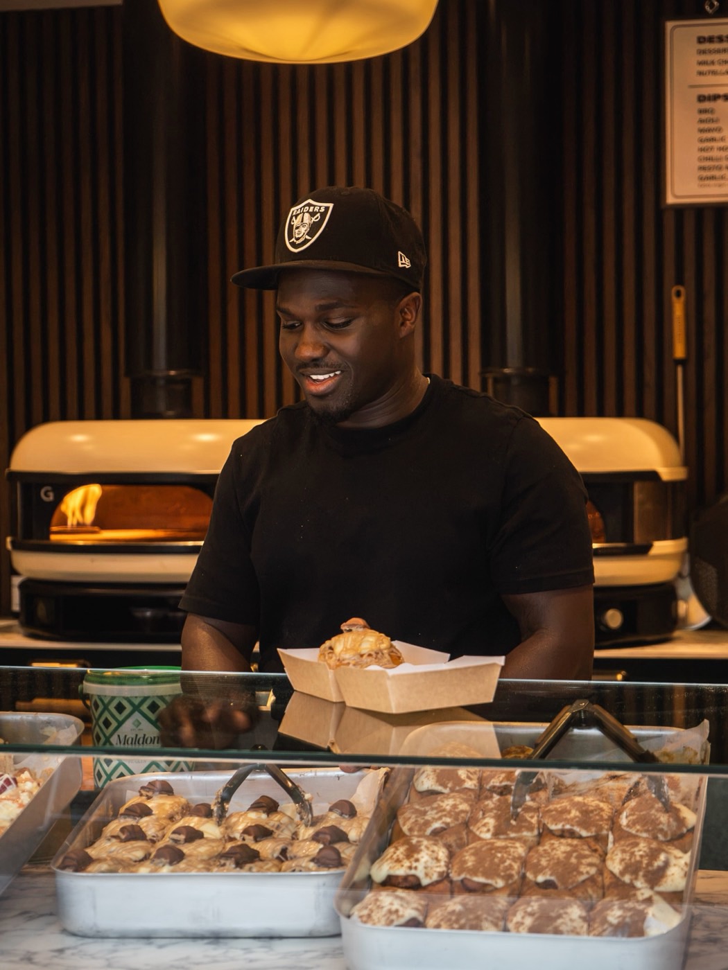 A member of staff boxing up a dessert at the counter, the pizza ovens lit in the background