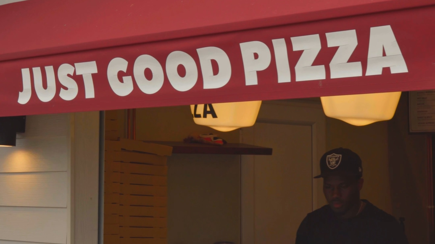 The red awning at Dough Boys, lettered Just Good Pizza, with a member of staff at the serving hatch underneath